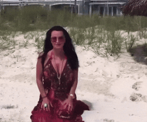 a woman in a red dress is kneeling on a beach