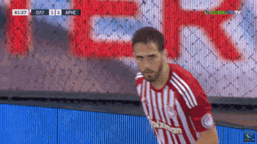 a soccer player in a red and white striped jersey stands on the field during a game