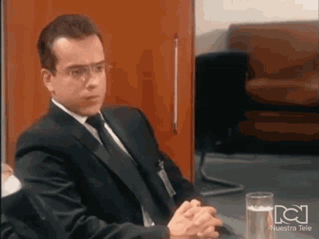a man in a suit and tie is sitting at a table with a glass of water in front of him .
