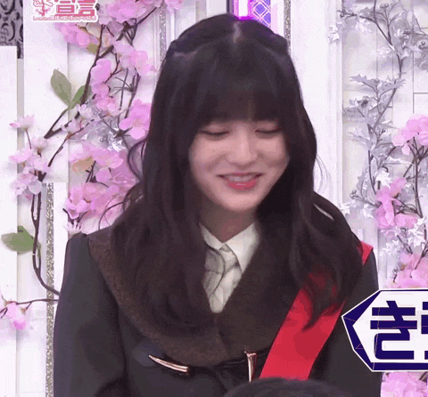 a girl with a red sash around her neck is smiling in front of a wall with pink flowers .