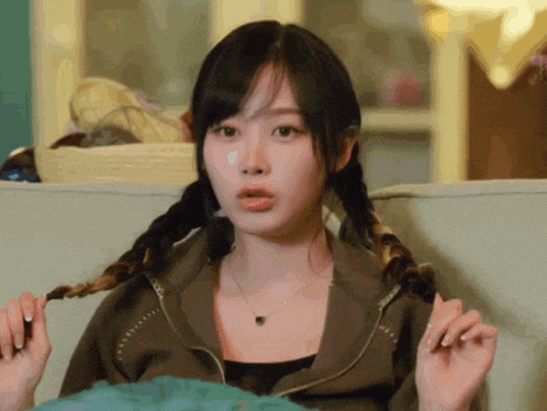 a woman with pigtails is sitting on a couch and making a funny face .