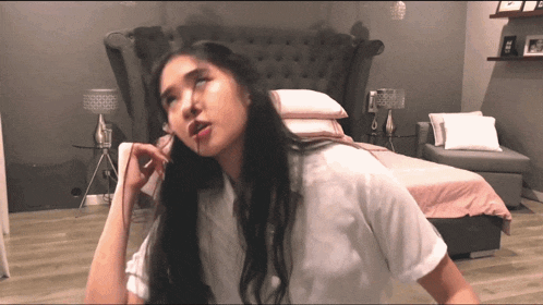 a woman in a white shirt is standing in front of a bed in a bedroom