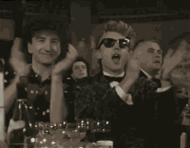 a group of people are sitting at a table with glasses of wine and applauding .