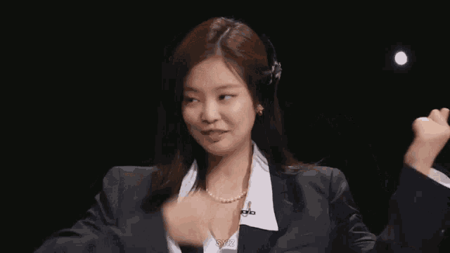 a woman in a suit and pearl necklace is laughing with her hands in the air