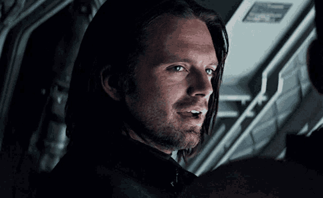 a close up of a man 's face with a beard and long hair in a dark room