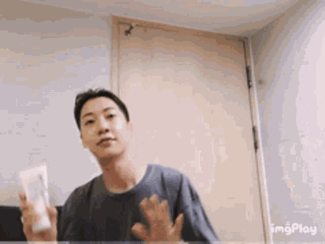 a man in a gray shirt is holding a bottle of lotion in front of a door ..