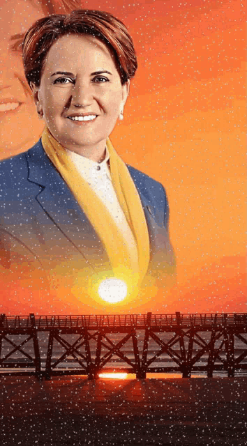 a woman in a blue jacket and yellow scarf is smiling in front of a bridge at sunset