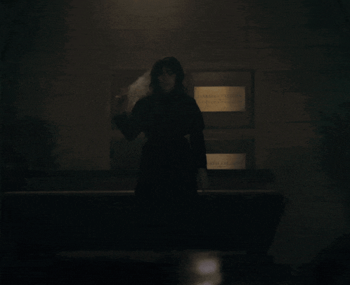 a woman in a black dress is standing in the dark under a light