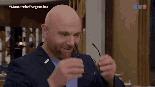 a bald man in a suit is holding a pair of glasses in his hands
