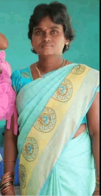 a woman wearing a blue and yellow saree stands in front of a green wall