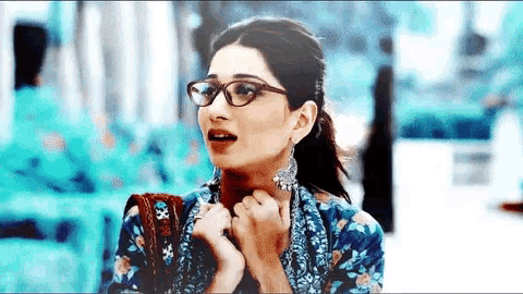 a woman wearing glasses and a blue shirt holds her hands to her face