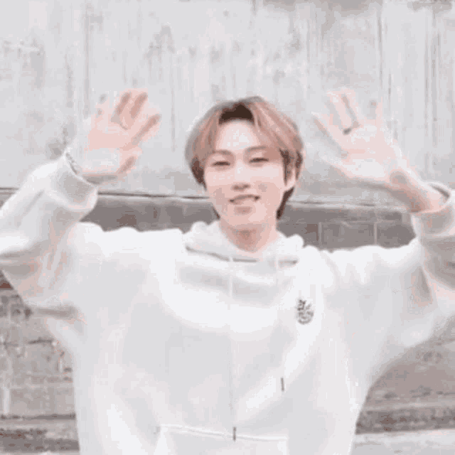 a young man is wearing a white hoodie and making a peace sign with his hands .