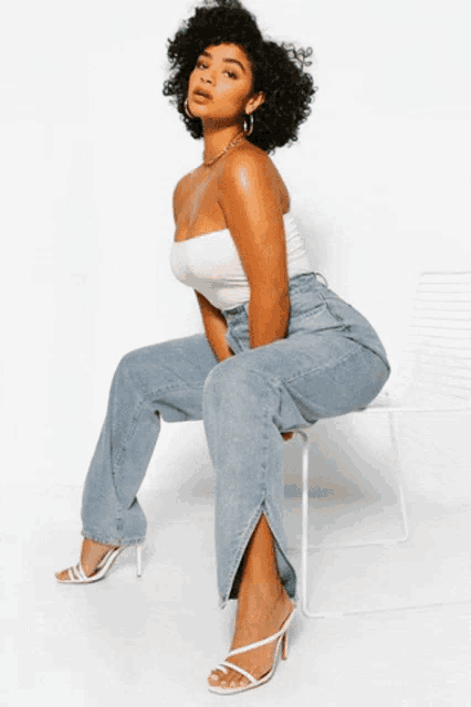 a woman is sitting on a stool wearing a white top and blue jeans