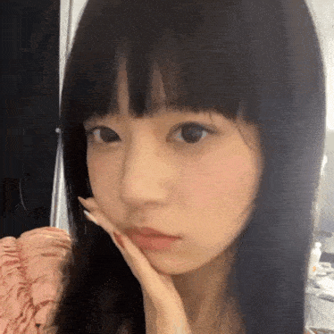 a young girl with long black hair is taking a selfie with her hand on her face .