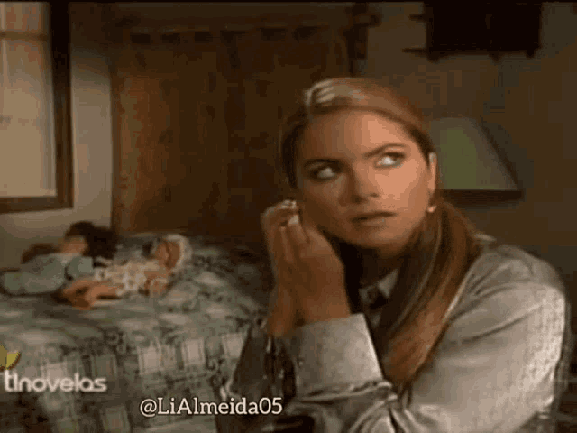 a woman is sitting in a room with a doll laying on a bed behind her .