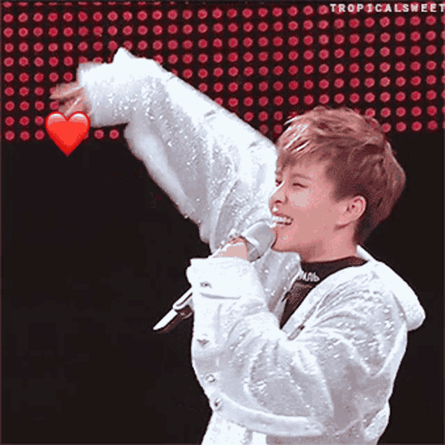a person holding a microphone in front of a heart that says tropicalsweet on it