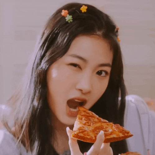 a girl with flowers in her hair is eating a slice of pepperoni pizza