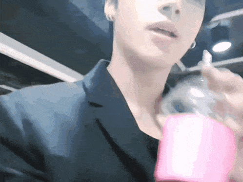 a man in a black suit is holding a pink bottle .