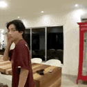 a man in a maroon shirt is standing in a living room with a red cabinet .