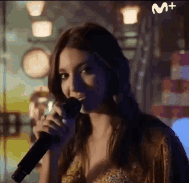 a woman is singing into a microphone with the letter m above her head