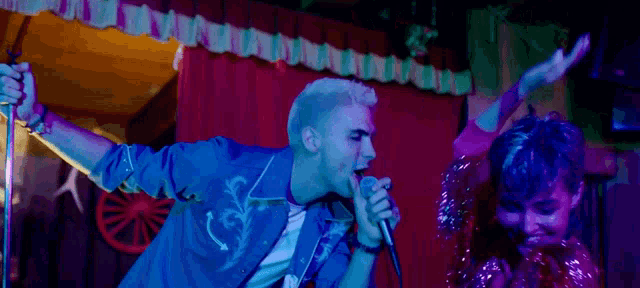 a man is singing into a microphone while a woman stands behind him