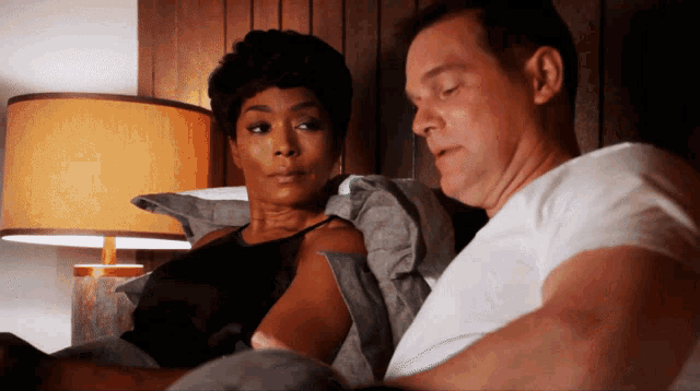 a man and a woman are laying in bed with a lamp in the background