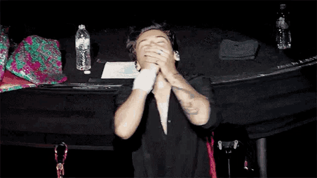 a man is covering his mouth with his hands while sitting on a stage in front of a table .