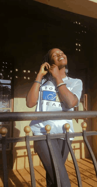 a woman wearing a tommy jeans t-shirt smiles while standing on a balcony