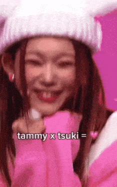a woman wearing a pink sweater and a white hat with bunny ears is smiling .