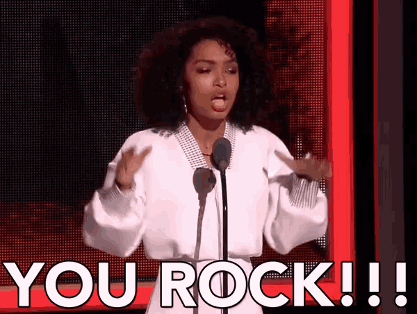 a woman stands in front of a microphone and says " you rock !! "