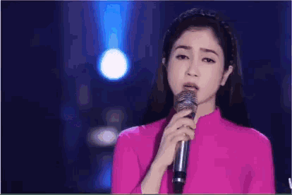 a woman in a pink dress singing into a microphone with the word không in white letters
