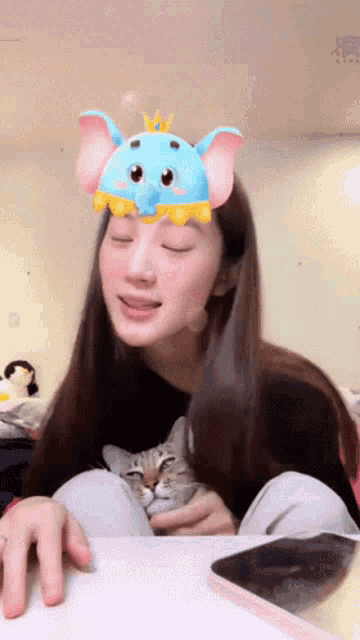 a woman wearing a blue elephant hat holds a cat in her lap