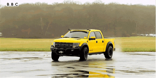 a yellow ford truck is on a wet road