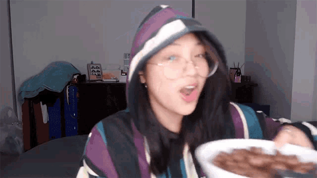a woman wearing a hoodie and glasses is eating cereal