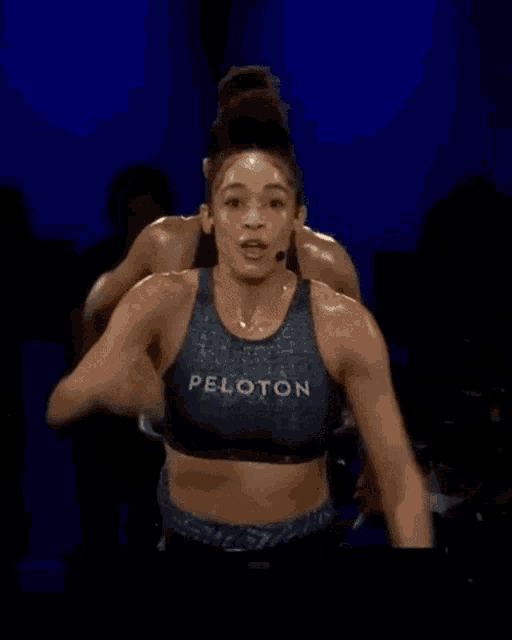 a woman wearing a peloton tank top is riding a bike .