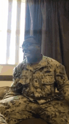 a man in a us marines uniform is sitting on a bed in front of a window .