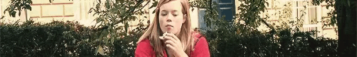a girl in a red shirt is blowing bubbles in front of a bush