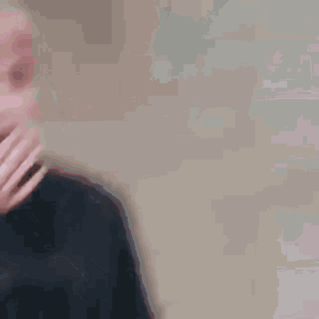 a man with pink hair and a black shirt is covering his mouth with his hand .