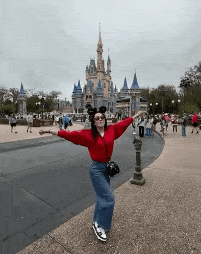 a woman is standing in front of a castle with her arms outstretched in front of it .