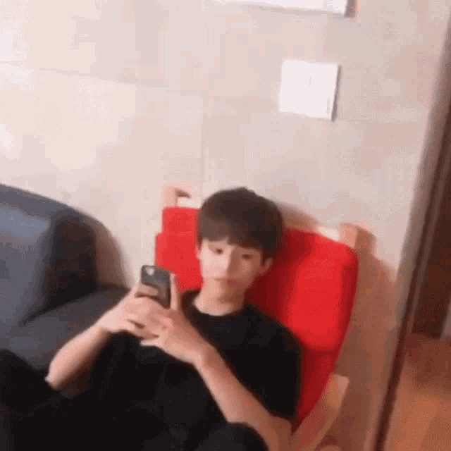 a young man is sitting in a red chair using a cell phone .