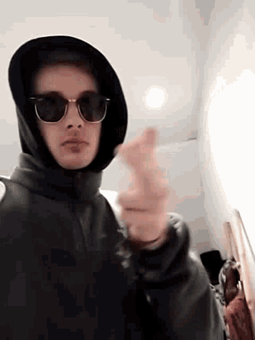 a man wearing sunglasses and a hood is smoking a cigarette .