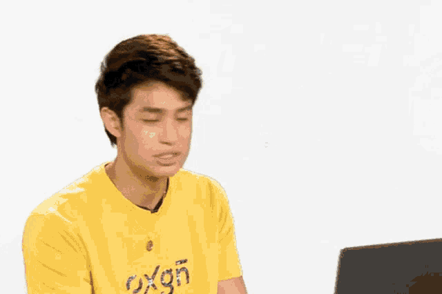 a young man wearing a yellow shirt is sitting in front of a wall with the word friend written on it .