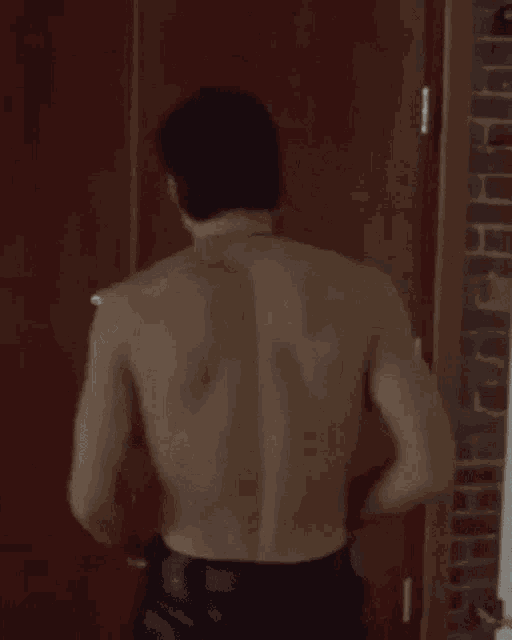 a man without a shirt is standing in a jail cell behind bars .