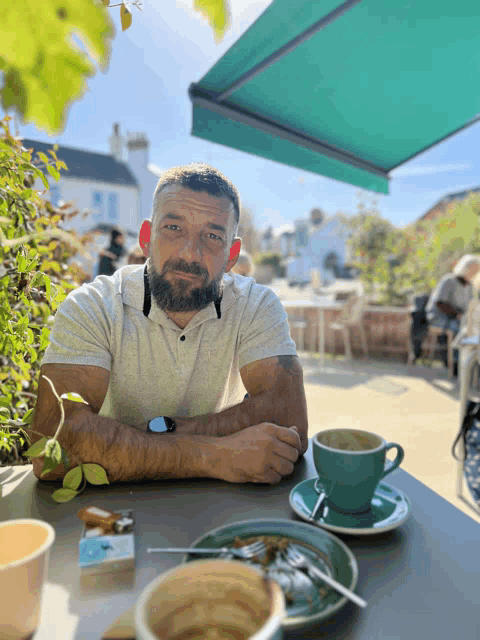 a man sits at a table with two cups of coffee and a cigarette