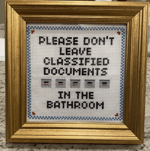 a cross stitch sign that says please don 't leave classified documents in the bathroom