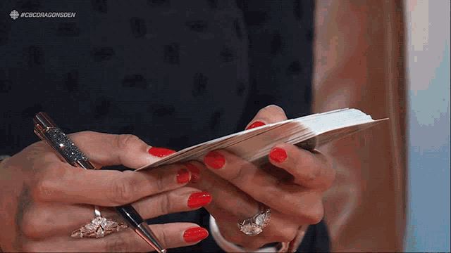 a woman with red nails holds a pen and a piece of paper
