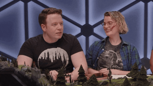 a man and a woman are sitting at a table with trees in front of them