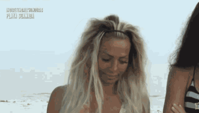 a woman with blonde hair is standing on a beach next to another woman