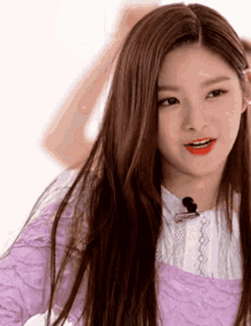 a woman with long brown hair is wearing a purple top and a microphone .
