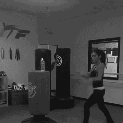 a black and white photo of a woman doing a karate kick in a gym .